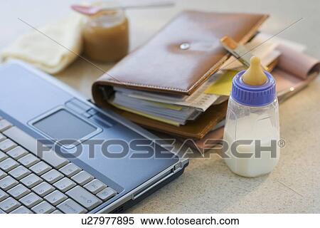 Stock Photography - Laptop, planner and baby bottle on table. Fotosearch