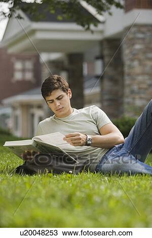 Stock Image - Male college student reading in grass. Fotosearch