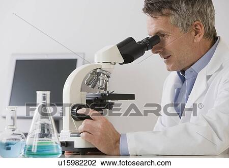 Stock Image - Male scientist looking in microscope. Fotosearch