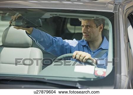 Picture - Man adjusting rear view mirror in car. Fotosearch