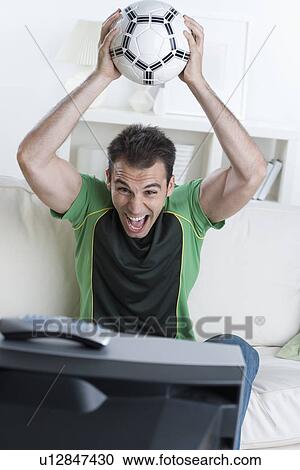 Man cheering and holding soccer ball while watching television View Large Photo Image Stock Image - Man cheering and holding soccer ball while watching television. Fotosearch
