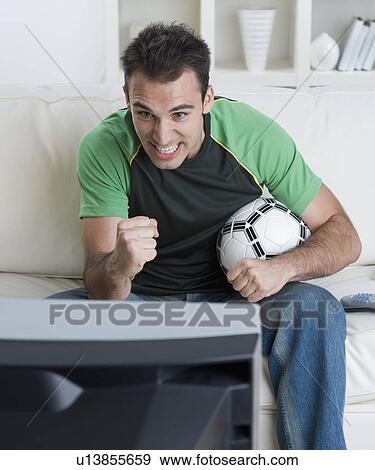Stock Photo - Man holding soccer ball and watching television. Fotosearch