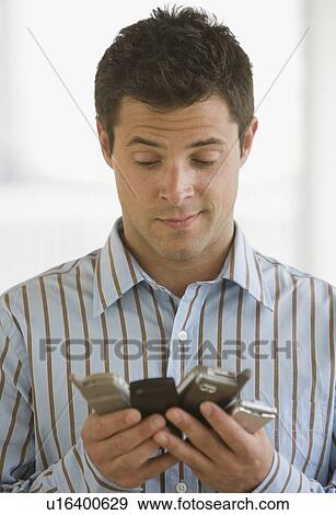 Stock Photo - Man looking at multiple cell phones. Fotosearch