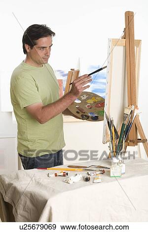 Stock Photo - Man painting at easel indoors. Fotosearch