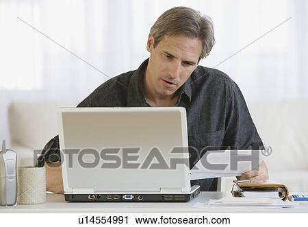 Stock Image - Man paying bills on laptop. Fotosearch