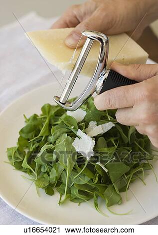 Stock Image - Man shaving cheese onto salad. Fotosearch