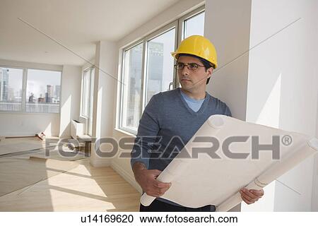 Man wearing hard hat and holding blueprints in house View Large Photo Image Stock Image - Man wearing hard hat and holding blueprints in house. Fotosearch