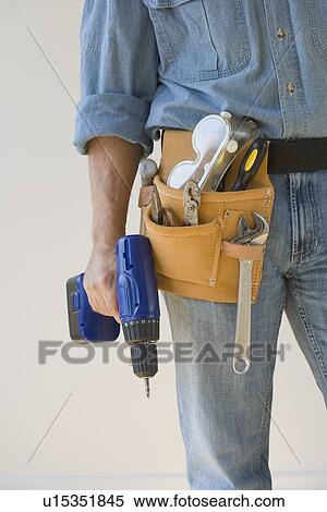 Stock Photography - Man wearing tool belt and holding drill. Fotosearch