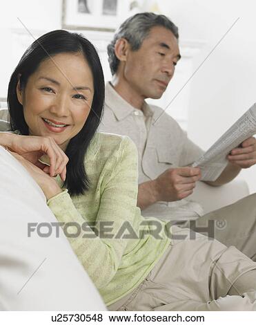 Stock Photo - Middle-aged Asian couple sitting on sofa. Fotosearch