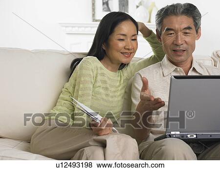 Middle-aged Asian couple sitting on sofa with laptop View Large Photo Image Stock Photo - Middle-aged Asian couple sitting on sofa with laptop. Fotosearch