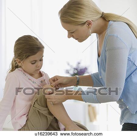 Stock Image - Mother bandaging daughter’s knee. Fotosearch