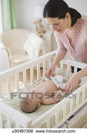 Stock Photograph - Mother changing baby’s diaper. Fotosearch
