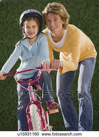 Stock Image - Mother helping daughter ride bicycle. Fotosearch