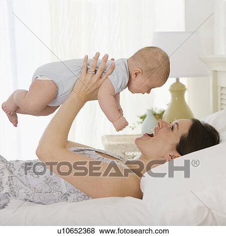 Stock Photo - Mother playing with baby on bed. Fotosearch