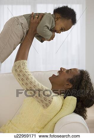 Stock Image - Mother playing with baby on sofa. Fotosearch