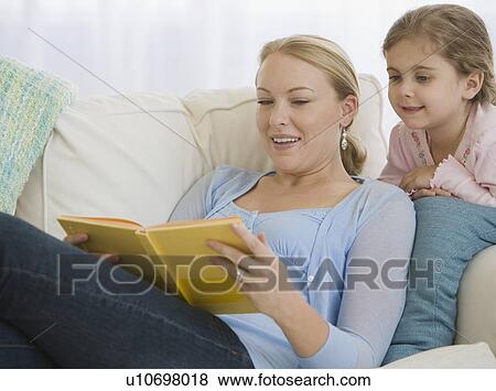 Stock Photo - Mother reading to daughter on sofa. Fotosearch
