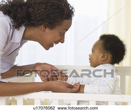 Stock Image - Mother smiling at baby in crib. Fotosearch