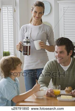 Stock Image - Mother smiling at father and son at breakfast table. Fotosearch