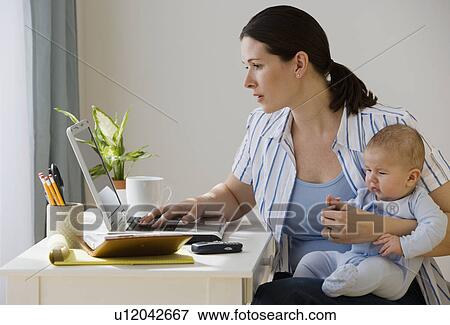 Mother typing on laptop and holding baby View Large Photo Image Stock Photo - Mother typing on laptop and holding baby. Fotosearch