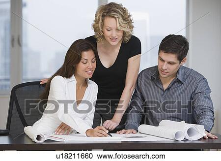 Stock Image - Multi-ethnic businesspeople looking at blueprints. Fotosearch