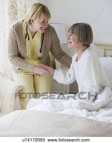 Stock Image - Nurse helping senior woman out of bed. Fotosearch