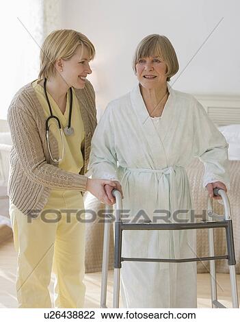 Stock Image - Nurse helping senior woman use walker. Fotosearch