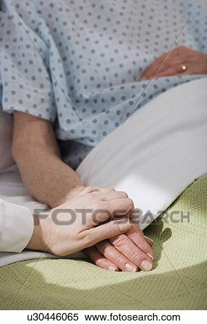 Stock Photography - Nurse holding senior woman’s hand in hospital. Fotosearch