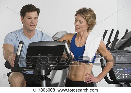Personal trainer assisting man on stationary bike View Large Photo Image Stock Photo - Personal trainer assisting man on stationary bike. Fotosearch