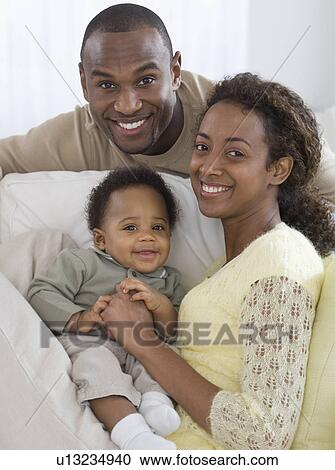 Stock Image - Portrait of parents and baby on sofa. Fotosearch