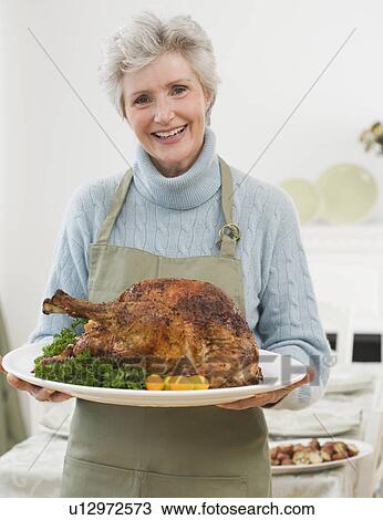Stock Image - Portrait of senior woman holding Thanksgiving turkey. Fotosearch
