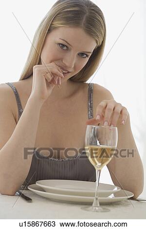 Stock Image - Portrait of woman at table with glass of wine. Fotosearch