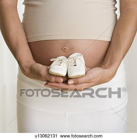 Pregnant woman holding baby shoes next to stomach View Large Photo Image Stock Image - Pregnant woman holding baby shoes next to stomach. Fotosearch