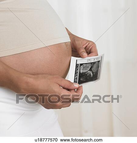Pregnant woman holding ultrasound next to stomach View Large Photo Image Stock Image - Pregnant woman holding ultrasound next to stomach. Fotosearch