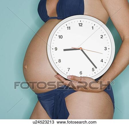 Pregnant woman holding wall clock View Large Photo Image Stock Image - Pregnant woman holding wall clock. Fotosearch