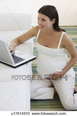 Stock Image - Pregnant woman looking at laptop. Fotosearch