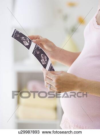 Stock Image - Pregnant woman looking at ultrasound printout. Fotosearch