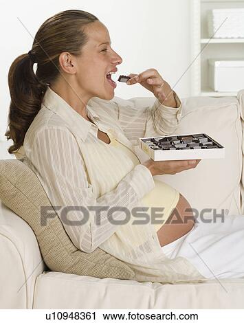 Pregnant woman on sofa eating box of chocolates View Large Photo Image Stock Image - Pregnant woman on sofa eating box of chocolates. Fotosearch