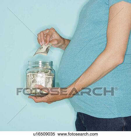Stock Photography - Pregnant woman putting money in jar. Fotosearch