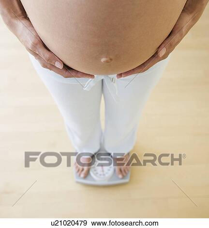 Stock Photo - Pregnant woman standing on scale. Fotosearch