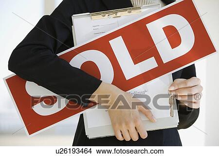 Picture - Real Estate agent holding clipboard and Sold sign. Fotosearch