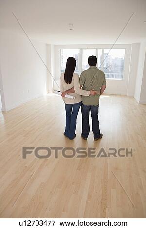 Stock Photo - Rear view of couple with blueprints in empty room. Fotosearch