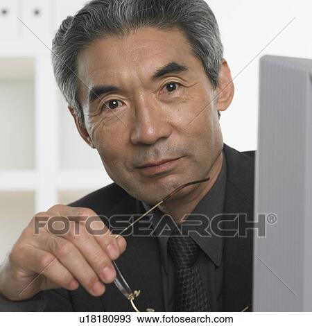 Stock Image - Senior Asian businessman holding eyeglasses. Fotosearch