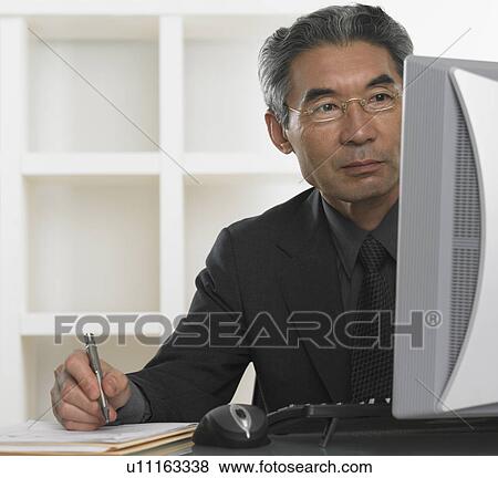 Senior Asian businessman looking at computer and writing View Large Photo Image Stock Photo - Senior Asian businessman looking at computer and writing. Fotosearch