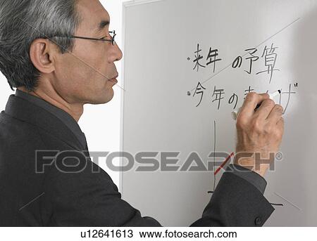 Stock Image - Senior Asian businessman writing on white board. Fotosearch