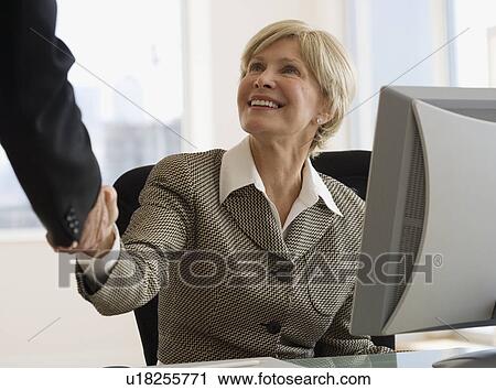 Stock Image - Senior businesswoman shaking hands at desk. Fotosearch