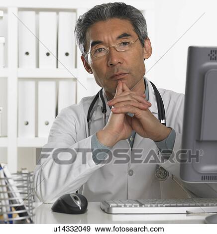 Senior male doctor sitting at computer View Large Photo Image Stock Photo - Senior male doctor sitting at computer. Fotosearch