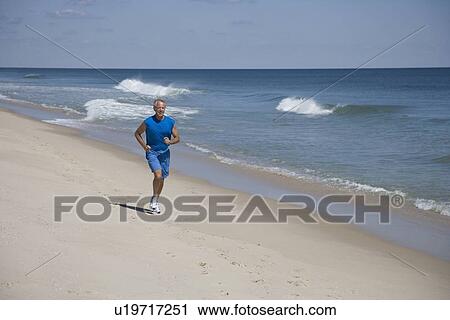 Stock Image - Senior man jogging on beach. Fotosearch