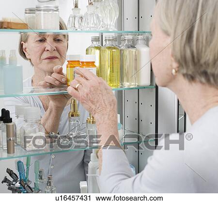 Stock Image - Senior woman looking in medicine cabinet. Fotosearch
