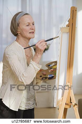 Stock Photo - Senior woman painting on easel. Fotosearch