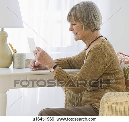 Stock Photo - Senior woman reading letter at desk. Fotosearch